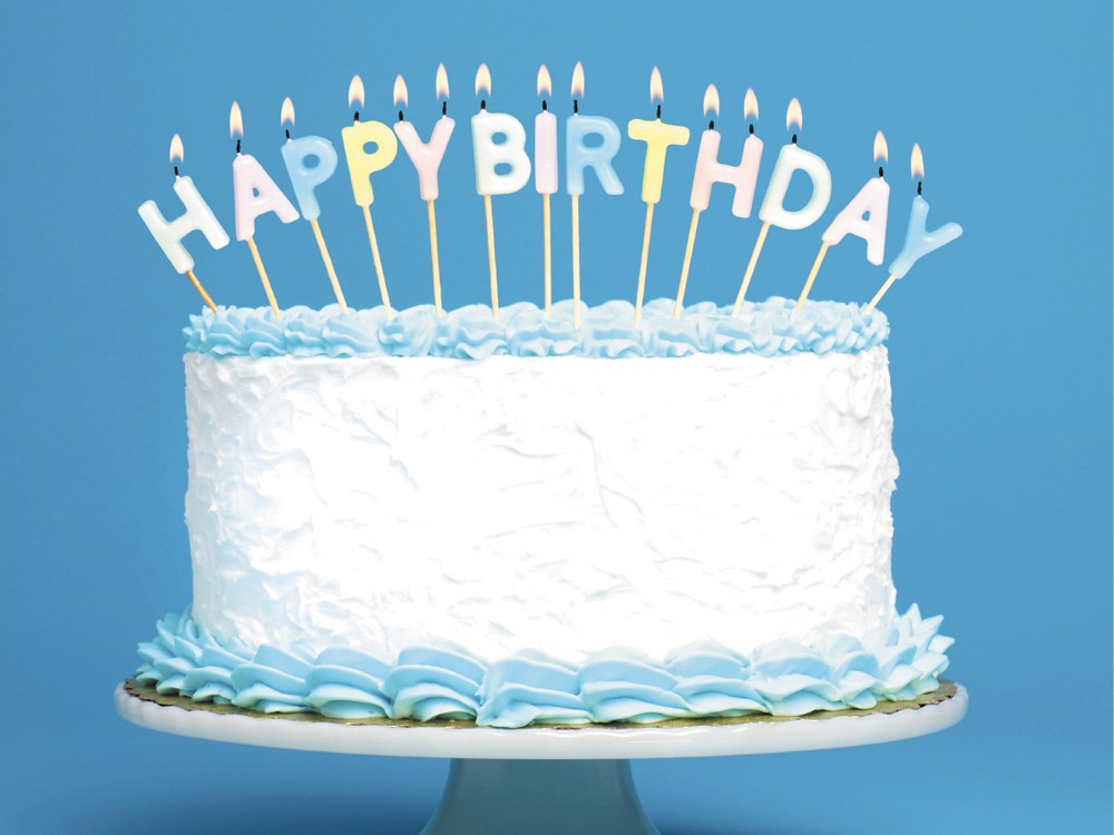 a white and blue birthday cake with candles reading 'happy birthday'